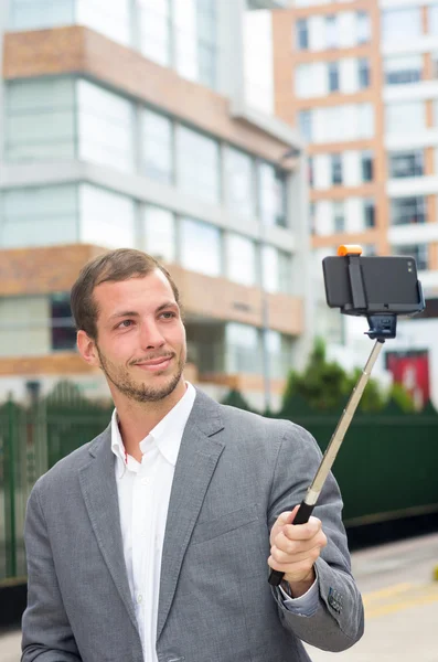 Man formella kläder poserar med selfie pinne i stadsmiljö — Stockfoto