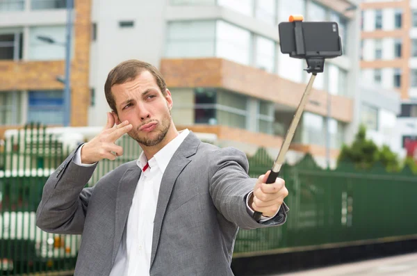 Man bär högtidsdräkt poserar med selfie pinne i stadsmiljö med höger hand för att göra en signal — Stockfoto