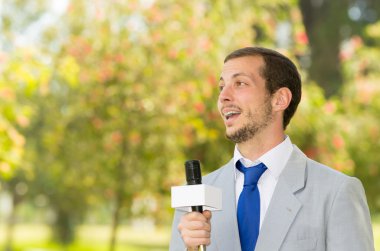 Açık havada çalışan Parkı çevre holding mikrofon canlı yayın ışık gri takım elbise giymiş başarılı yakışıklı erkek haber muhabiri