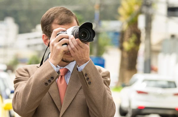 Exitoso fotógrafo masculino atractivo con traje marrón que trabaja al aire libre en el tráfico entorno urbano celebración de la cámara — Foto de Stock