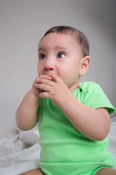 Niedlicher kleiner Junge in grüner Kleidung, der vor der Kamera sitzt und den Mund mit Händen bedeckt und zur Seite starrt — Stockfoto
