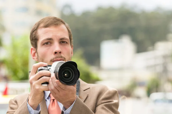 Exitoso fotógrafo masculino atractivo con traje marrón que trabaja al aire libre en el tráfico entorno urbano celebración de la cámara —  Fotos de Stock