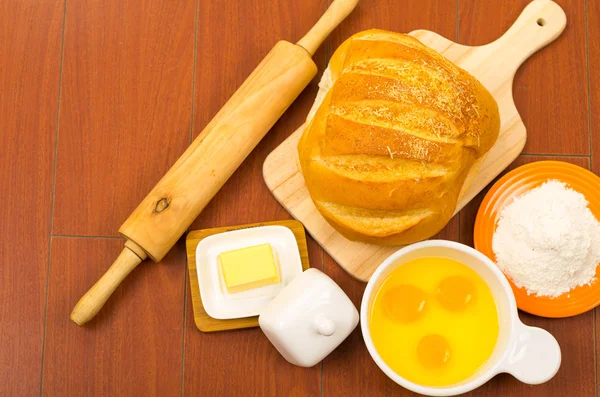 Rolo de pão, queijo, ovos rachados em uma tigela e farinha exibida na superfície de madeira de cima ângulo — Fotografia de Stock