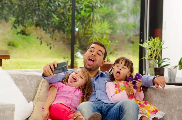 Retrato familiar del padre y dos hijas sentadas juntas en un sofá posando para selfie sin lengua —  Fotos de Stock