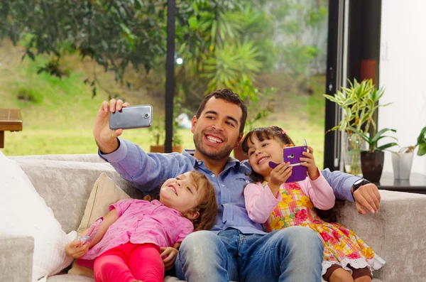 Family portrait of father and two daughters sitting together in sofa posing for selfie cozy family style — Stock Photo, Image