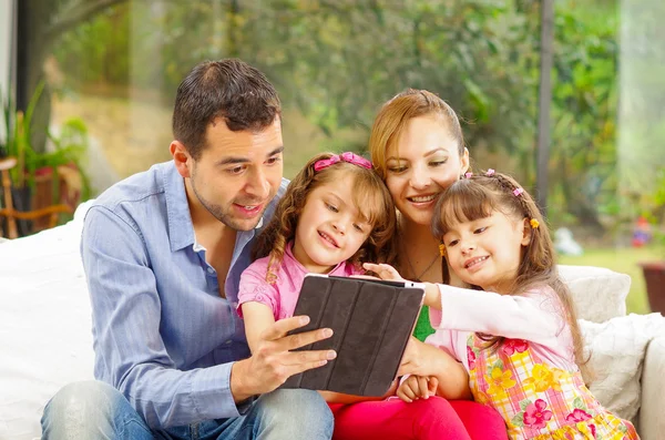 Familienporträt von Vater, Mutter und zwei Töchtern, die zusammen auf dem Sofa sitzen und fröhlich mit Tablet spielen — Stockfoto