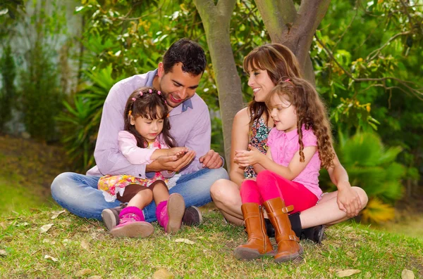 Family portrait of father, mother and two daughters sitting together in garden environment enjoying each others company — Stock Photo, Image