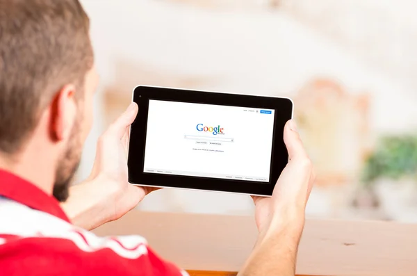 Молодой человек, пользующийся планшетным компьютером, просматривает сайт Google — стоковое фото