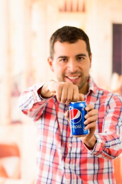 Attractive young man smiling opening a Pepsi Cola can