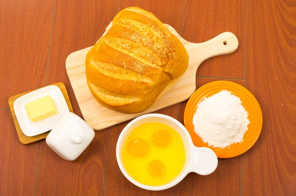 Pane ben colorato posto sulla superficie di legno accanto alla ciotola bianca con uova, formaggio e farina . — Foto Stock