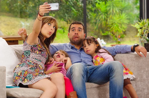 Portrait de famille de père, mère et deux filles assis ensemble dans le canapé posant pour selfie faire des visages drôles Images De Stock Libres De Droits
