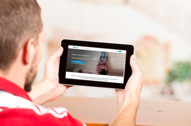 Young man using tablet computer looking at Paypal website