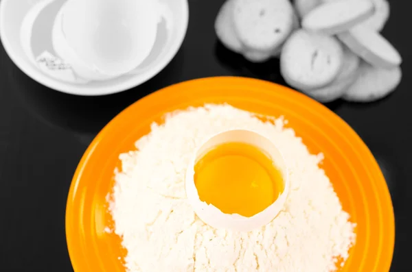 Strong yellow colored plate with flour crater containing cracked egg, black and white sorroundings shot from above side angle — Stock Photo, Image