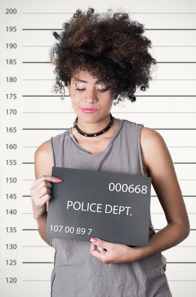 Hispanic brunette rebel model afro like hair wearing grey sleeveless shirt holding up police department board with number as posing for mugshot, careless facial expression — Stock Photo, Image