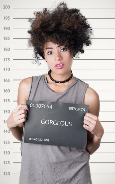 Hispanic brunette rebel model afro like hair wearing grey sleeveless shirt holding up police department board with number as posing for mugshot, careless facial expression — Stock Photo, Image
