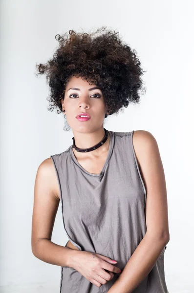 Hispanic brunette model with afro like hair wearing casual grey sleeveless shirt posing for camera white background — стокове фото