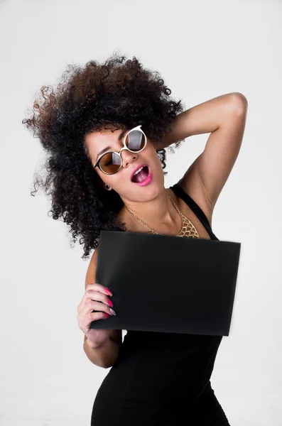 Hispanic model wearing black sexy dress and sunglasses holding blank board with right arm, left touching hair posing — Stockfoto