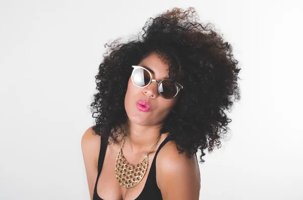 Headshot hispanic model wearing black dress, golden necklace, sunglasses and curly hair making kiss lips for camera — Stock fotografie