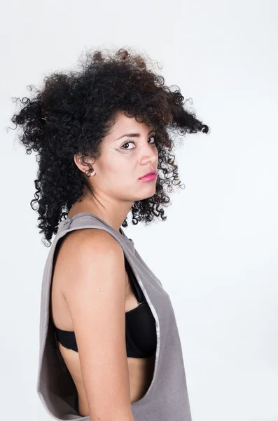 Modelo morena hispana con el pelo desordenado usando camisa gris sin mangas que mira infeliz en la cámara desde el ángulo del perfil, concepto mugshot —  Fotos de Stock