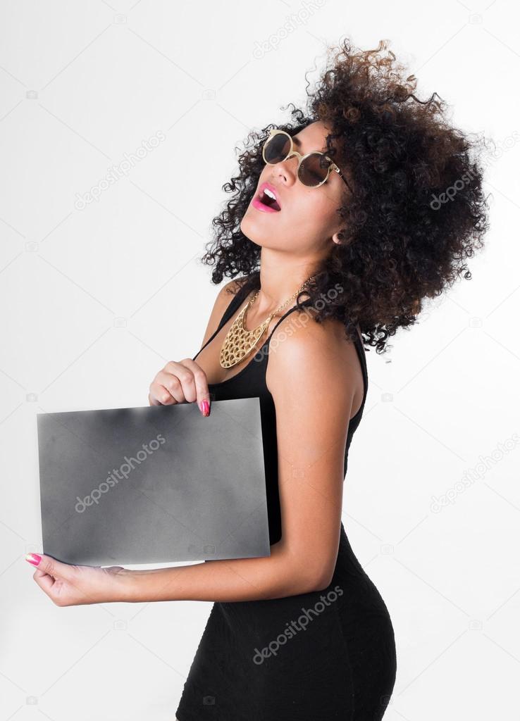 Hispanic model wearing black sexy dress and sunglasses holding blank board looking upwards, shot from profile angle