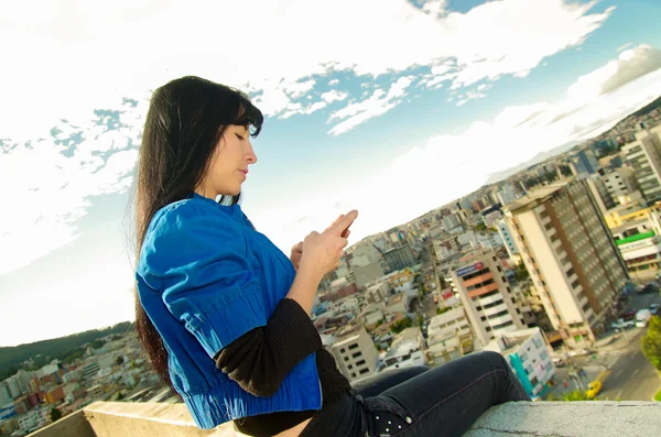 Beautiful young girl sitting on the roof using her cell phone — Stock fotografie