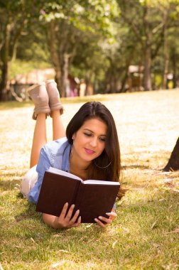 Brunette model lying on grass happily reading a book