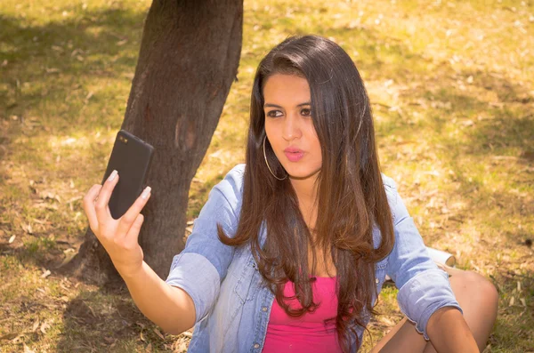 Pretty brunette model posing for a selfie while in park environment — Stockfoto