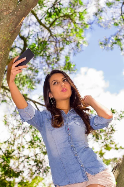 Pretty brunette model posing for a selfie while in park environment — Stockfoto