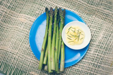Demet taze kuşkonmaz ve tereyağı daldırma, kenevir masa örtüsü mavi bir plaka yerleştirilir biberiye.