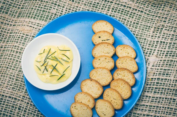 Piccole fette di pane e burro di rosmarino su piatto blu — Foto Stock