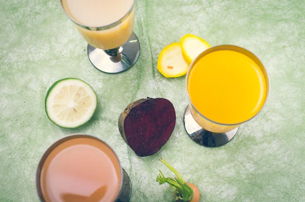 Organic delicious cups of orange juice placed on table next to lime, zucchini, beetroot and carrot — Stock Photo, Image