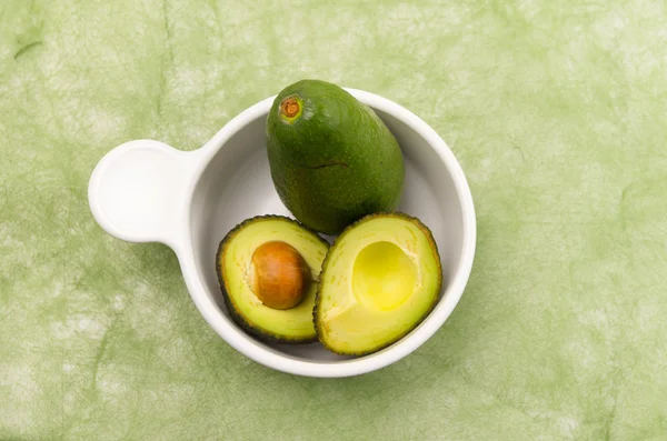Felgekleurde twee avocado's in een witte kom met een gesneden in helften — Stockfoto