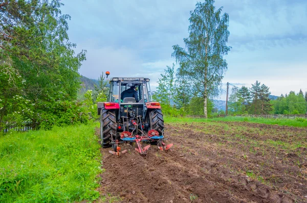 Tractor working in field opening preparing soil for planting vegetables, shot from behind angle
