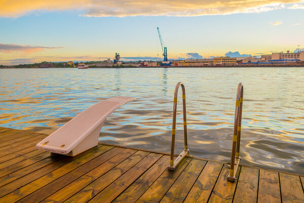 OSLO, NORWAY - 8 JULY, 2015: Diving board mounted on wooden surface above water at Aker Brygge pier area during sunset hour