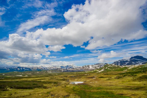 VALDRES, NORUEGA - 6 DE JULIO DE 2015: Impresionante naturaleza en Valdresflya, paisaje verde cubierto se extiende tan lejos como la vista puede ver con manchas de nieve y lagos bajo el hermoso cielo azul —  Fotos de Stock