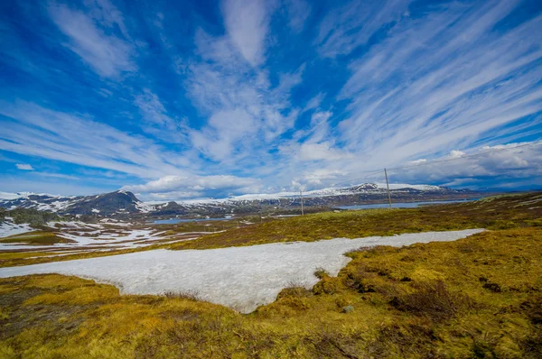 VALDRES, NORUEGA - 6 DE JULIO DE 2015: Impresionante naturaleza en Valdresflya, paisaje verde cubierto se extiende tan lejos como la vista puede ver con manchas de nieve y lagos bajo el hermoso cielo azul — Foto de Stock