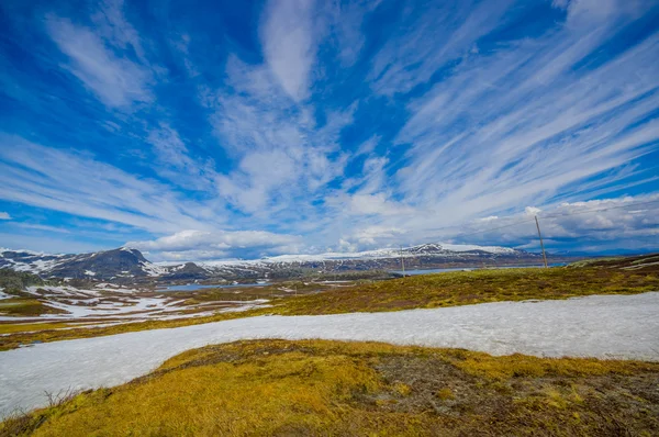 VALDRES, NORUEGA - 6 DE JULIO DE 2015: Impresionante naturaleza en Valdresflya, paisaje verde cubierto se extiende tan lejos como la vista puede ver con manchas de nieve y lagos bajo el hermoso cielo azul — Foto de Stock