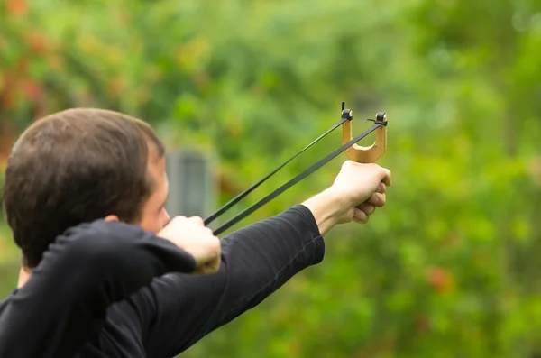 Handsome man concentrated aiming  a slingshot at park having fun — Zdjęcie stockowe