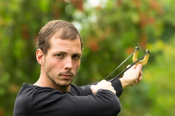 Handsome man concentrated aiming  a slingshot at park having fun — Stock Photo, Image