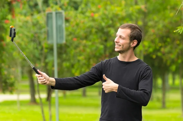 Hispanic man posing with selfie stick in park environment smiling — Zdjęcie stockowe