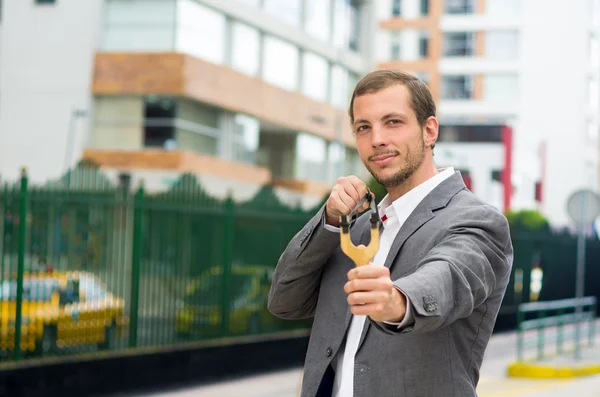Handsome buisness man concentrated aiming a slingshot at urban city background — Stock Photo, Image