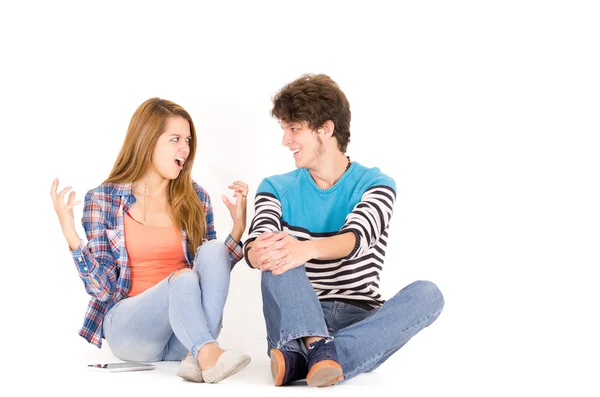 Portrait attractive young happy couple in love, man and woman, isolated over white background sitting on floor looking to each other, she is intense. — Stock fotografie