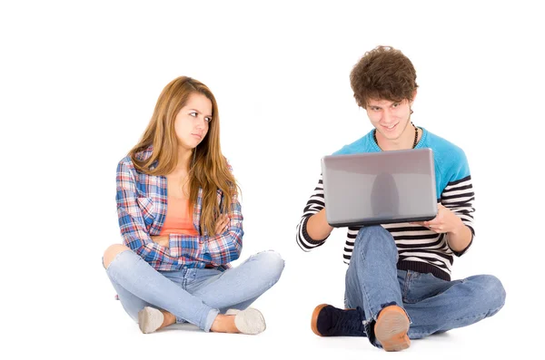 Retrato de atraente jovem casal apaixonado homem e mulher isolado sobre fundo branco sentado no chão, ele olha para o computador enquanto ela está louca — Fotografia de Stock