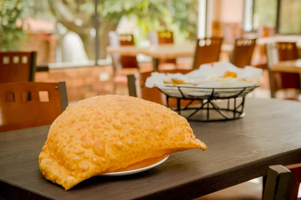 Amplia empanada sobre mesa de madera junto a canasta de comidas latinas típicas, refrescante entorno de restaurante — Foto de Stock