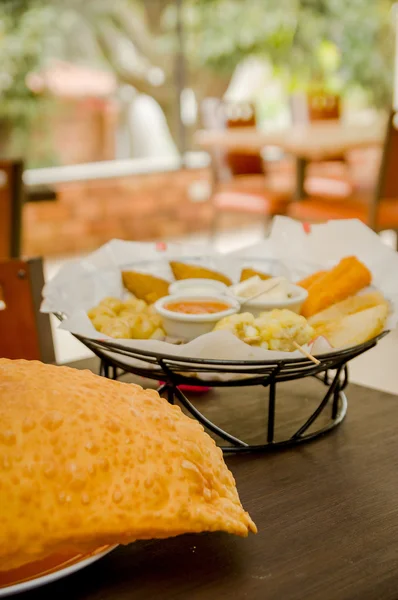 Große Empanada auf Holztisch neben Korb mit typisch lateinischen Speisen, erfrischendes Restaurant-Ambiente — Stockfoto