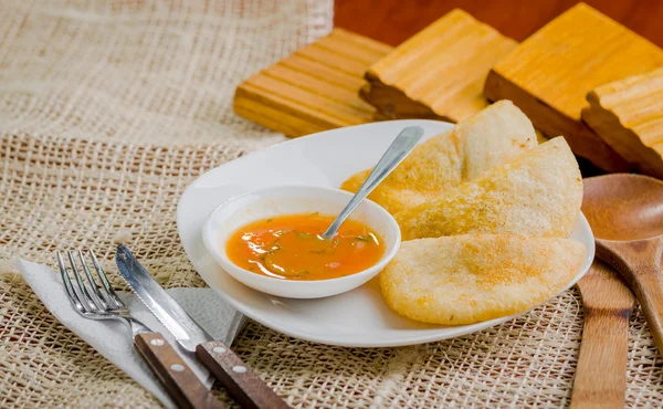 Drei Empanadas schön auf weißem Teller neben kleiner Salsaschüssel und rustikalem Hintergrund angeordnet — Stockfoto