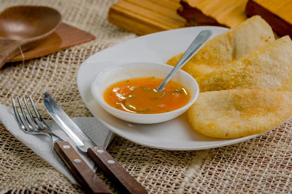 Drei Empanadas schön auf weißem Teller neben kleiner Salsaschüssel und rustikalem Hintergrund angeordnet — Stockfoto