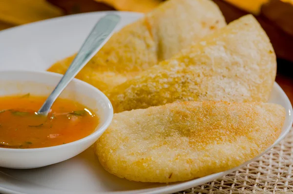 Tre empanadas ben disposti su piatto bianco accanto a piccola ciotola di salsa e sfondo rustico — Foto Stock