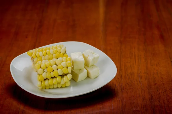 Placa blanca con la mitad de mazorca de maíz cocida acostada junto a trozos de queso cuadrado fresco estable — Foto de Stock