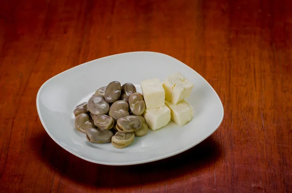 Mucchio di abba cotti accanto a piccoli pezzi quadrati stabili formaggio su piatto bianco — Foto Stock